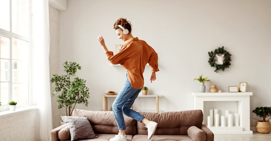 Frau tanzt mit Kopfhörern auf Couch
