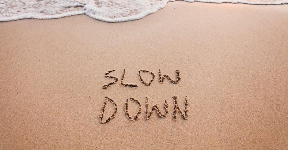 Schriftzug "Slow down" im Sand