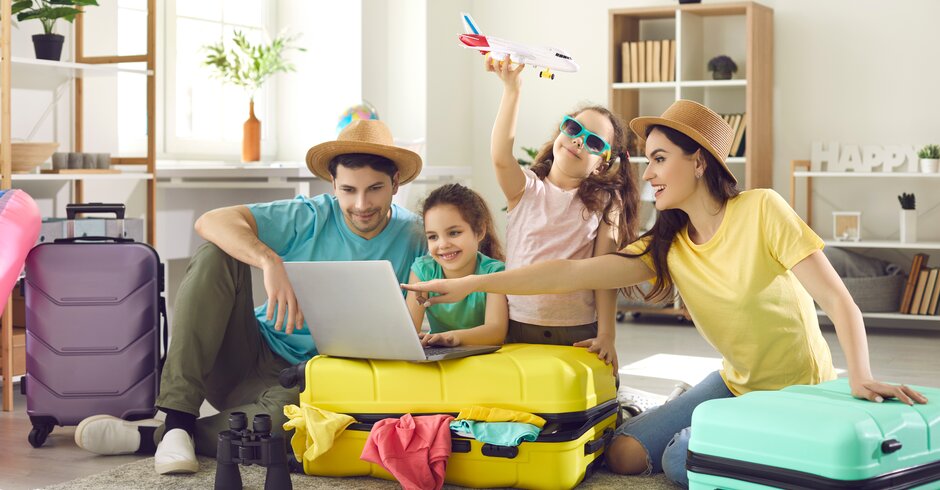 Familie mit zwei Kindern sitzt neben Reisekoffern und bereit sich auf den Urlaub vor