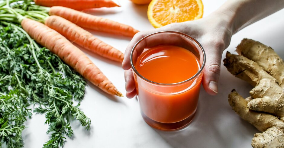 Oranger Smoothie dekorativ angerichtet mit Karotten, Orangen und Ingwer drum herum