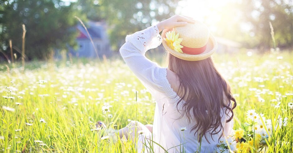 Frau mit Sonnenhut sitzt in Wiese