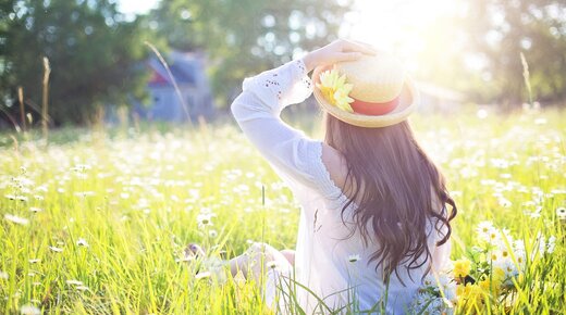Frau mit Sonnenhut sitzt in Wiese