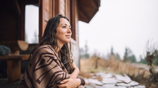 Frau vor einem Haus genießt Ausblick in die Natur