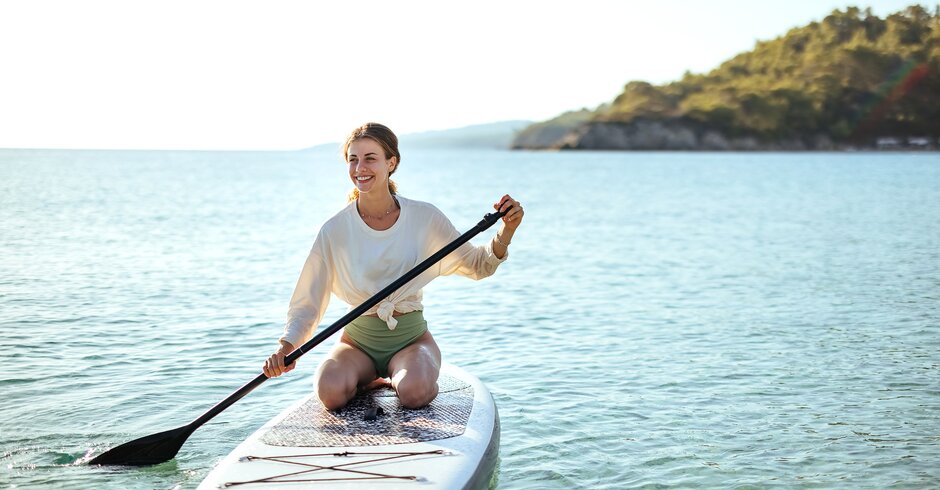 Frau kniet auf Stand-up-Paddleboard am See