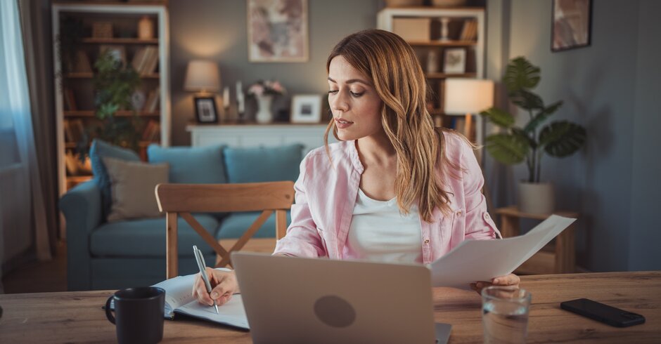 Frau sitzt am Tisch mit Notebook und Notizbuch