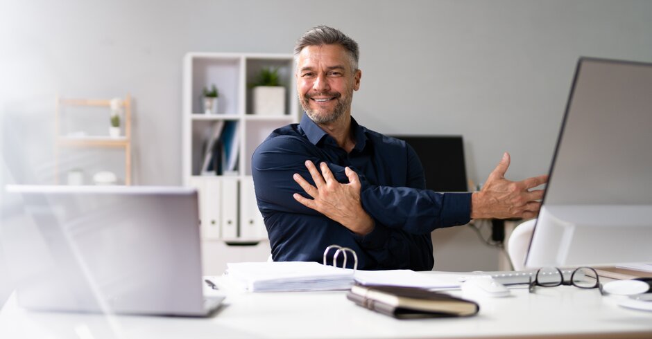 Angestellter dehnt seinen Arm am Schreibtisch